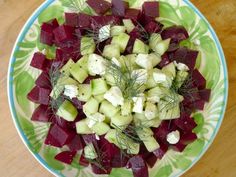 a green and white plate with beets, cucumbers, and feta cheese