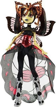 a doll is dressed in black and pink with butterfly wings on her head, sitting on top of a round object