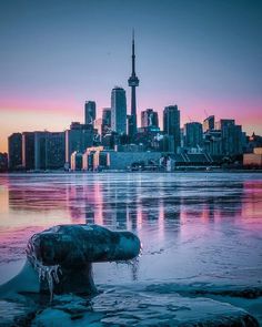 the city skyline is reflected in the water at sunset, with ice floes on the ground