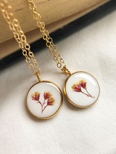 Resin pendant with pressed flowers. Each pendant is filled with layers of white and clear resin. The white effect gives it a more vintage look. Get yours today! Please keep in mind that a few tiny bubbles may appear in your piece.  Necklace chain, jump rings, and clasps are 14k gold filled. Choose from 3 different lengths.  Gold stainless steel pendant trays. Size inside pendant: 12mm Jewelry Care:  Avoid submerging jewelry in water Store in a cool/dry place away from direct sunlight Do not wear White Birth Flower Pendant Necklace, Elegant White Necklace With Pressed Flowers, Nature-inspired White Birth Flower Necklace, White Round Pendant Necklace With Nature-inspired Style, White Flower Necklace With Nature-inspired Style, White Flower-shaped Nature-inspired Necklace, White Flower Pendant Necklace With Pressed Flowers, White Nature-inspired Necklace With Pressed Flowers, Vintage White Jewelry With Pressed Flowers