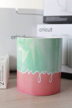 a pink and green coffee mug sitting on top of a table next to a white box