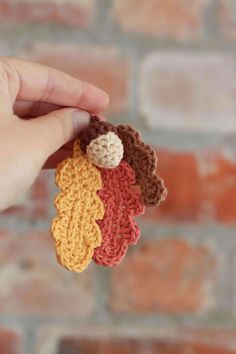 a hand holding three crocheted leaves in front of a brick wall