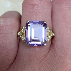 An 18k yellow gold ring centering an emerald-cut 5.33 carat amethyst, set in prongs. On either side of the amethyst is a geometric design that is set with round brilliant cut diamonds. Additional round brilliant diamonds line the shoulders. This ring is decorated with an open-work under-gallery. The approximate dimensions of the amethyst are 12.00mm x 10.00mm. This ring can be resized to any finger size at no extra cost. If you have any questions about the Lucille ring, please feel free to conta Antique Ruby Ring, Estate Diamond Jewelry, Amethyst Set, 18k Yellow Gold Ring, Perfect Engagement Ring, Design Set, Yellow Gold Ring, Ruby Ring, Brilliant Diamond