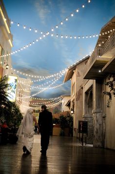 the bride and groom are walking down the hall under string lights at their wedding reception