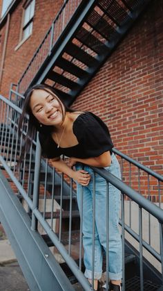 a woman standing on the stairs in front of a brick building smiling at the camera