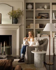 a woman sitting in a chair next to a fire place with candles on the mantle