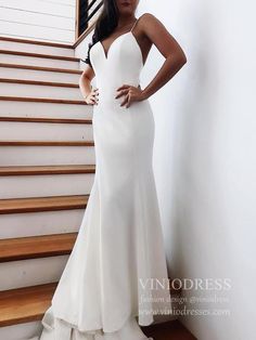 a woman standing in front of some stairs wearing a white wedding dress with deep v - neck