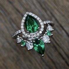 an emerald and diamond ring sitting on top of a wooden table