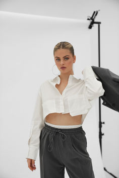 a woman standing in front of a white backdrop with her hands on her hips and wearing grey pants