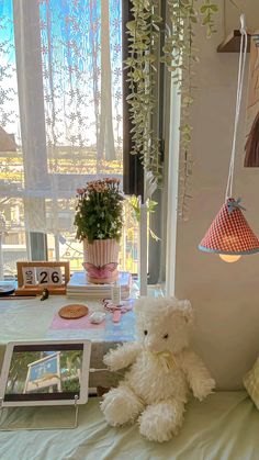 a white teddy bear sitting on top of a bed next to a framed photograph and potted plant