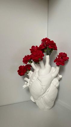 a white vase filled with red flowers sitting on top of a table next to a wall