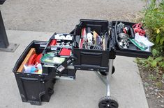 two black boxes filled with assorted items sitting on top of a sidewalk next to a trash can