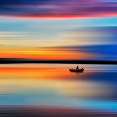 a boat floating on top of a large body of water under a colorful sky at sunset