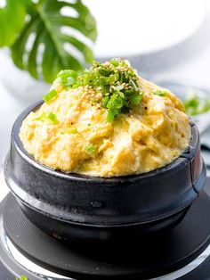 a black plate topped with mashed potatoes on top of a wooden table next to a potted plant