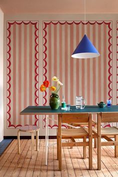 a dining room table with chairs and a blue lamp hanging from the ceiling in front of striped wallpaper