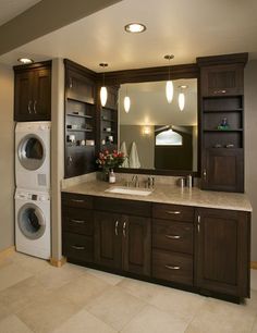 a washer and dryer in a large bathroom with dark wood cabinets, marble counter tops, and tile flooring