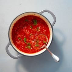 a pot filled with red sauce and garnished with green leaves on the side