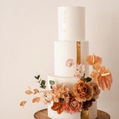 a three tiered white cake with flowers on top and gold trim around the edge