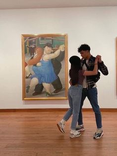 two people walking in an art gallery with paintings on the wall