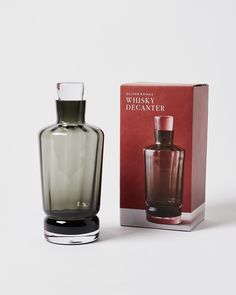 an empty glass bottle next to a box on a white surface with a red background