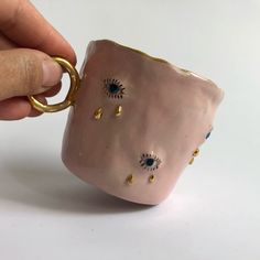 a hand is holding a ceramic cup with gold and blue eyes on it's side