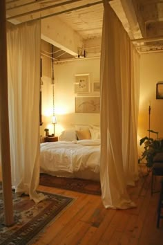 a bed with white sheets and drapes in a bedroom next to a wooden floor