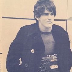 a young man holding an old typewriter in his right hand and looking at the camera