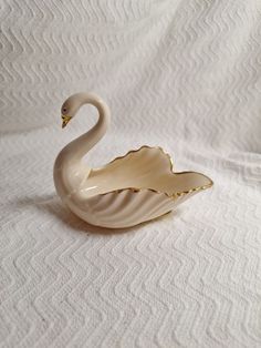 a white swan shaped dish sitting on top of a white tablecloth covered bed sheet