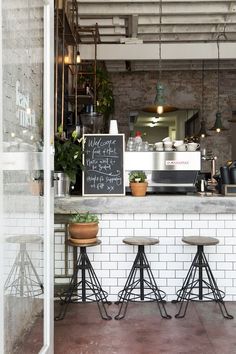 three stools in front of a bar with a chalkboard