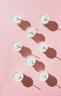 several clocks are arranged in the shape of faces on a pink background with shadow from one person's hand