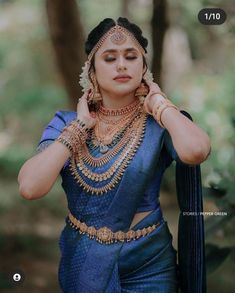 a woman in a blue sari with gold jewelry on her neck and hands behind her head