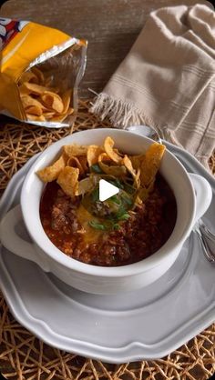 a white bowl filled with chili and tortilla chips on top of a plate