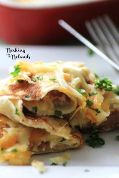 a white plate topped with lasagna covered in cheese and parsley next to a fork