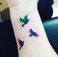 three birds flying in the air with green and red colors on their wrist tattoo design