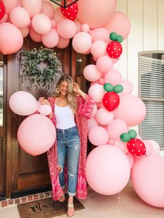 a woman standing in front of a door surrounded by pink balloons and strawberry shaped decorations