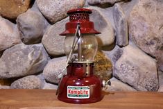 a red lantern sitting on top of a wooden table next to rocks and a stone wall