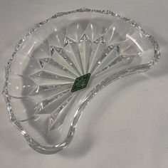 a clear glass dish on a white surface with a green label in the center and an intricate design