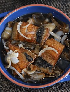 a blue bowl filled with meat and onions on top of a brown cloth covered table