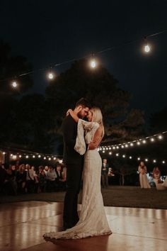 a bride and groom dance on the dance floor at their wedding reception with string lights in the background