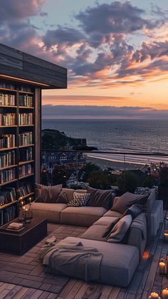 a living room with couches and bookshelves next to the ocean at sunset