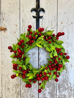 a wreath hanging on the side of a white wooden door with green leaves and red berries