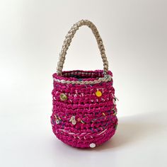 a small pink basket with buttons on the handle and handles, sitting against a white background