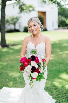 a woman in a wedding dress holding a bouquet and smiling at the camera while standing on grass