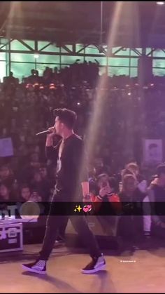 a man standing on top of a stage with a microphone in his hand and an audience behind him