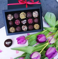 a box of chocolates sitting next to purple tulips