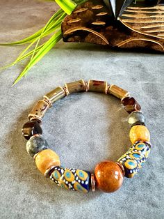 Brown ceramic tube beads , Ochre ceramic Focal bead, Blue n yellow Krobo Recycled glass beads, multicolor jasper gemstone beads, Faceted brown agate beads Men's/Unisex Bracelet  ------------------------------------- You'll catch yourself always stroking the smooth tube-shaped brown ceramic beads in this elegant bracelet. It's a soothing feel complemented by the eye-catching speckled Ochre ceramic focal bead flanked by the beautifully patterned matte Krobo recycled glass beads, followed by muted Beaded Bracelet Designs, Expensive Necklaces, Mens Bracelet Gold, Wooden Bead Jewelry, African Bracelet, Clothespin Diy Crafts, African Inspired Jewelry, Handmade Ceramic Jewelry, African Bracelets