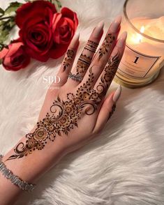 a woman's hand with henna on it next to a candle and roses