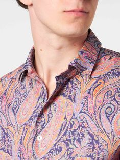 a man wearing a purple paisley shirt and black sunglasses with his head tilted to the side