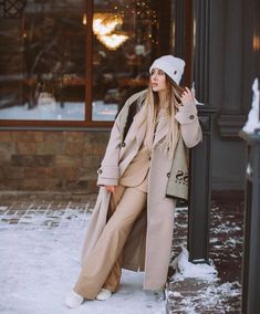 a woman leaning against a pole in front of a building wearing a hat and coat