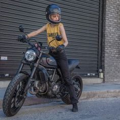 a woman sitting on top of a motorcycle in front of a garage with roller doors